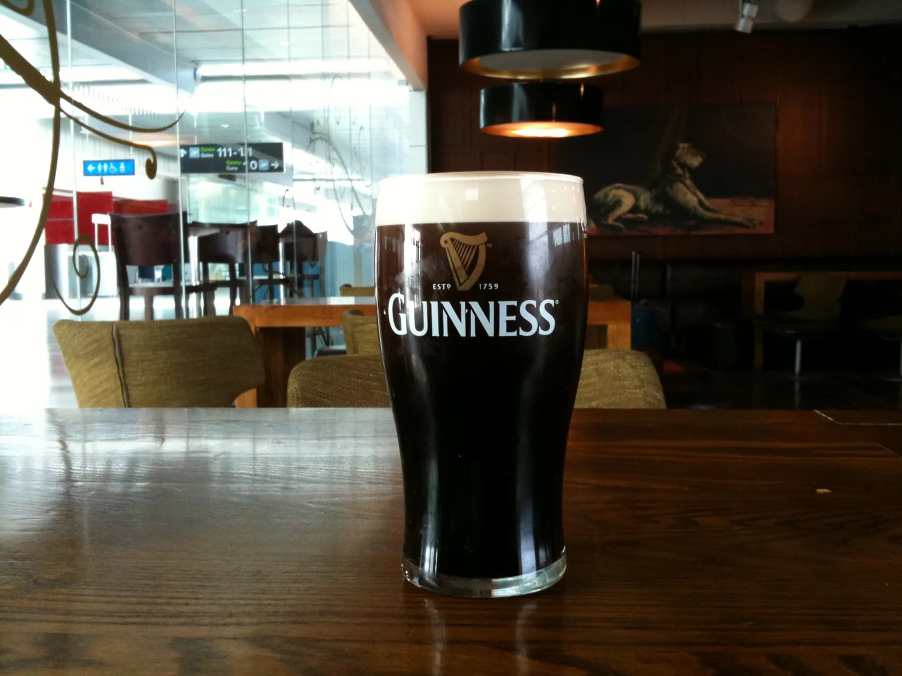 A settled pint of Guinness in a branded glass on a wooden table at a Dublin bar, its creamy head above the dark body