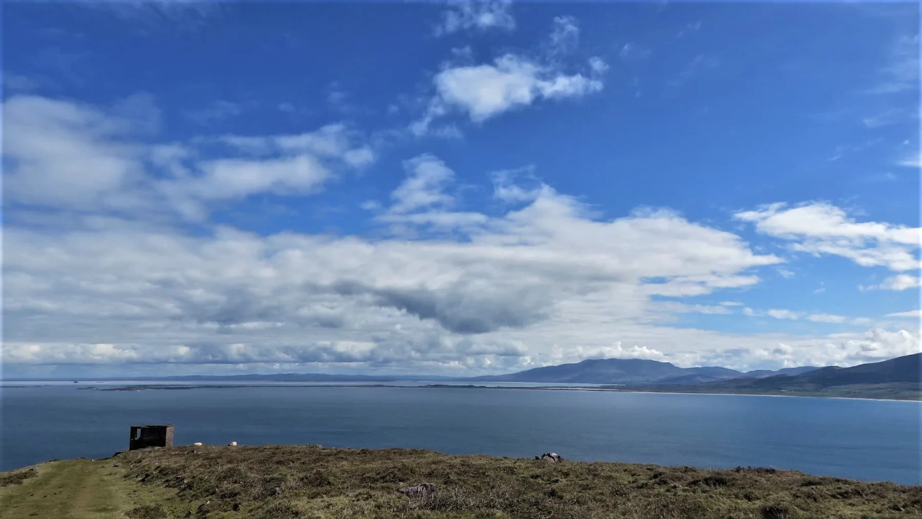 A wide view over Dingle Bay, County Kerry, under a big Irish sky of scattered cloud, with distant mountains across the water